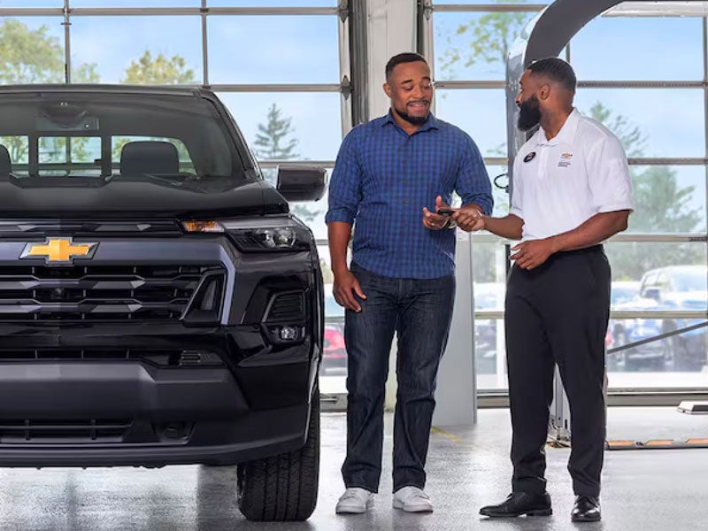 A photo of two people standing next to a Chevrolet truck